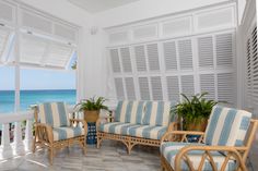 a living room filled with furniture next to an ocean side window covered in shutters