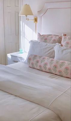 a bed with white sheets and pink pillows