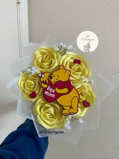 a hand holding a bouquet of yellow roses with winnie the pooh on it's side