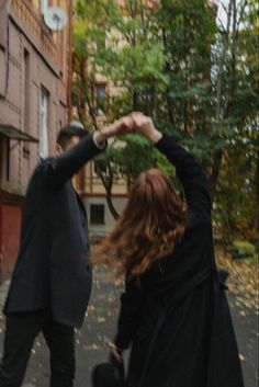 two people are walking down the street with their hands in the air and one person is holding his hat