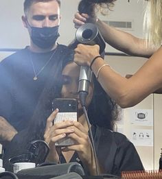 a woman is getting her hair styled by a man in a black shirt and mask