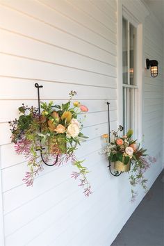 two wall mounted planters on the side of a house with flowers hanging from them