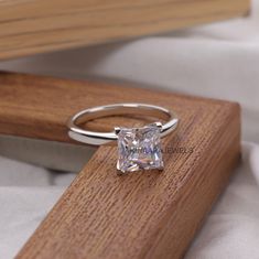 an engagement ring with a princess cut diamond set in 18k white gold on a wooden stand