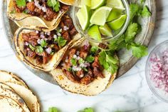 tacos with meat, onions and cilantro on a plate next to tortillas