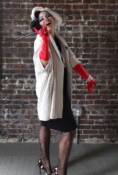 a woman wearing red gloves and holding a microphone in her hand while standing next to a brick wall