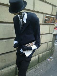 a mannequin dressed in a suit and top hat stands next to a building