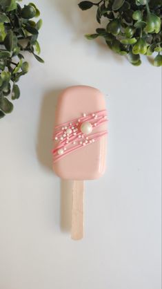 a pink lollypop with pearls and ribbon on it sitting next to some plants