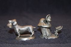 two silver figurines of dogs and a cat on a blue surface with a black background