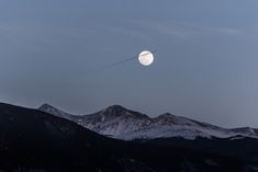 the moon is setting over mountains with a string attached to it's back end