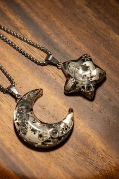 two silver necklaces with skulls on them sitting on a wooden table next to each other