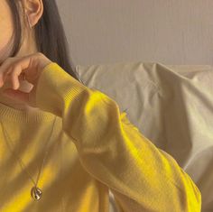 a woman wearing a yellow sweater is holding her hand to her ear