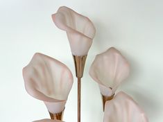 three pink glass flowers are hanging on a white wall in front of a light fixture