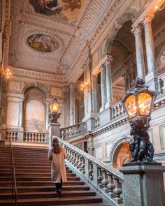 a woman is walking down the stairs in a large building with chandeliers and paintings on the walls