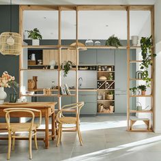 an open kitchen and dining room area with wooden tables, chairs and shelves filled with potted plants