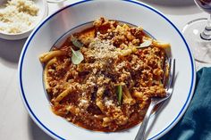 a white plate topped with pasta covered in meat and sauce next to two glasses of wine