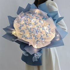 a woman is holding a blue and white paper bouquet with butterflies on the petals,