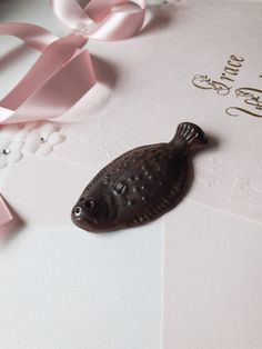 a card with a fish on it next to some pink ribbons and pearls in the background