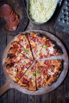 a pizza sitting on top of a wooden cutting board next to a pan filled with cheese