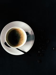 a cup of coffee sitting on top of a white saucer next to black beans