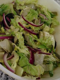 a salad with lettuce and onions in a white bowl on top of a table