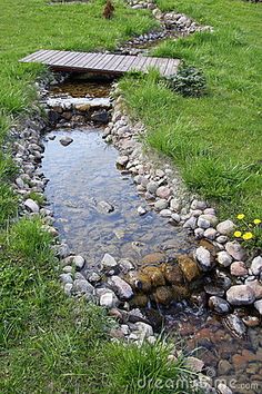 a small stream running through a lush green field next to a wooden bridge over water