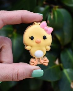 a hand holding a tiny yellow chick with a pink bow on it's head