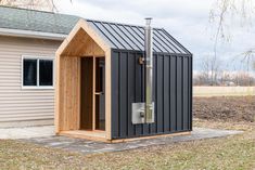 a small house with a metal roof and door on the side of it, in front of a field