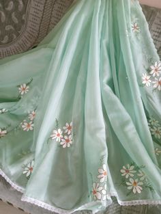 a green dress with white flowers on it sitting on a bed next to a pillow