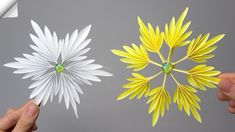 two paper flowers being held in one hand and the other with green stones on it