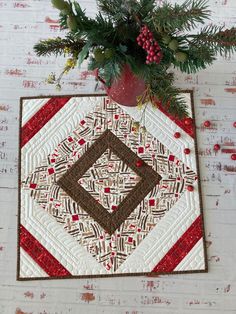 a quilted christmas ornament hanging on a brick wall next to a potted plant