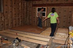 two people standing in a room that is being built with wooden boards and plywood