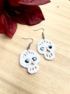 two white lace earrings with black beads on top of a wooden table next to a red flower