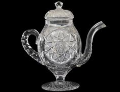 a clear glass teapot with a lid and handle on a black background, it appears to be in the shape of a flower ornament