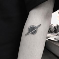 a small saturn tattoo on the left inner arm, with a black and white circle around it