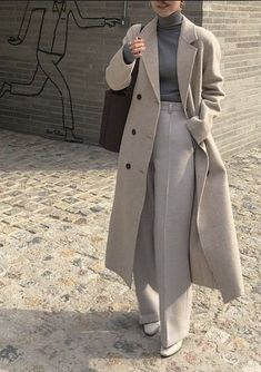 a woman is walking down the street with an umbrella in her hand and wearing a gray coat