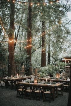 an outdoor dinner table set up in the woods with lights strung from trees and candles