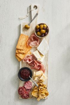 an assortment of cheeses, meats and olives on a cutting board with bread