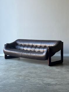 a black leather couch sitting on top of a cement floor next to a white wall