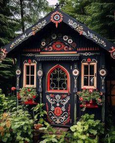 a black and red house in the middle of some trees with potted plants around it