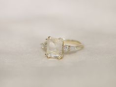 an engagement ring with a large stone surrounded by three small white diamonds on a plain surface