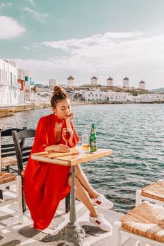 a woman sitting at a table with a bottle of wine in front of her and looking out over the water