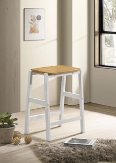 a wooden stool sitting on top of a hard wood floor next to a potted plant