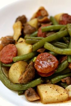 a white plate topped with green beans, potatoes and sausage