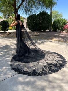 a woman wearing a long black veil standing in front of a tree with her back to the camera