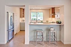 a kitchen with two stools next to an island in the middle of the room