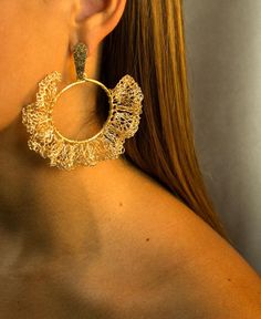 a close up of a woman wearing large gold hoop earrings with filigrees