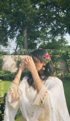 a woman in a white dress is holding her hand up to her face and looking into the distance