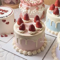 there are many cakes with strawberries on the top one is pink and white, the other is blue