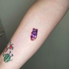 a small purple teddy bear tattoo on the left arm and wrist, next to an apple