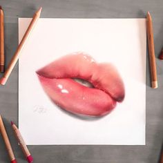 a pencil drawing of a pink lip on white paper with crayons around it